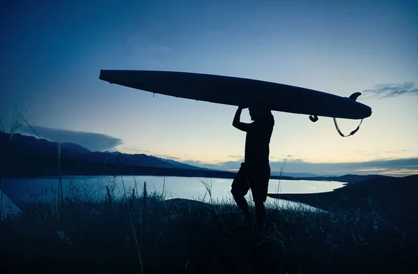 Man in silhouette holding SUP board on his head near lake at sunset in Kazakhstan. Stand up
