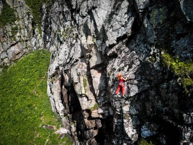 Kazakistan 'daki Tyan Shan dağlarında yüksek kayalara tırmanan kırmızı tişörtlü güçlü bir kadının robot resmi.