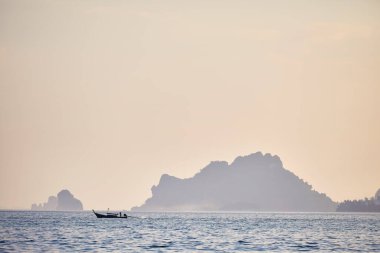 Traditional long tail in silhouette near tropical islands at sunset in Andaman Sea, Southern Thailand