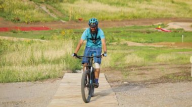 Mavi tişörtlü ve kasklı MTB motorcusu Enduro dağ parkında geziyor. Dağlarda dağ bisikleti.