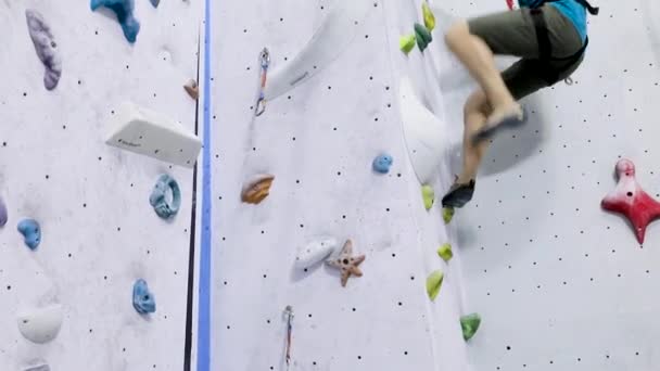 ロックシューズの男の足は 安全システムとロープで屋内岩壁に登るアップを閉じます — ストック動画