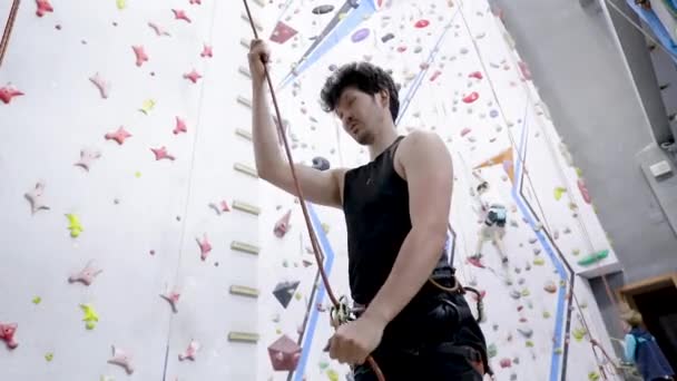 クライマーは 屋内ロックウォールでロープ屋外ライフスタイルスポーツによってブレーキを引く彼の登山パートナーを保護します — ストック動画