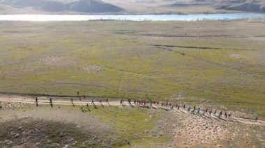 Gün batımında nehir ve tepelerin yanındaki tozlu köy yolunda yarışan kalabalığın insansız hava aracı görüntüsü. Güney Kazakistan 'daki Ili nehri yakınlarındaki bozkırda akan patika.