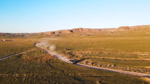 カザフスタンの日没時に春の緑の草原でイリ川の近くのほこりの多い道路で高速とバギー車のドライブのドローン撮影空中ビュー — ストック動画