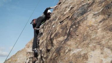 Mavi şortlu ve kasklı adam Kazakistan 'daki Ili Nehri' nde güvenli bir iple yüksek kayaya tırmanıyor.
