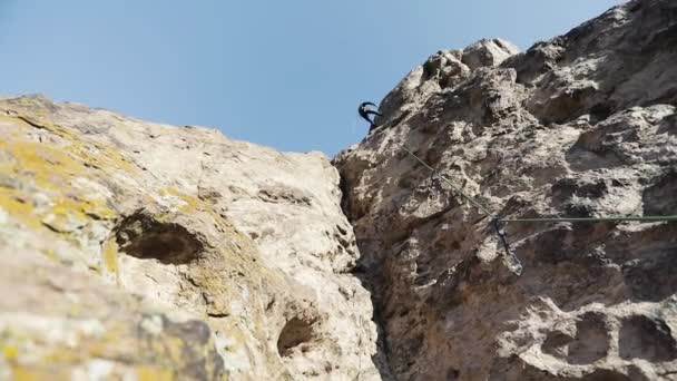 哈萨克斯坦伊犁河里 身穿蓝色短裙头戴安全帽的男子马拉松选手用锯齿状绳索爬上了高高的岩石 — 图库视频影像