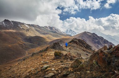 Mavi ceketli adam Hiker, sonbaharda dağ vadisinde bulutlu gökyüzüne karşı Rocky Hill yolunda yürüyor. Açık hava ve yürüyüş konsepti.