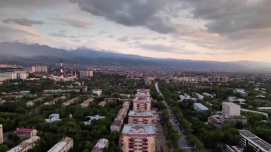 Gökdelen kulesinin hava aracı manzaralı manzarası ve Almaty şehrinde gün batımında mor bulutlu kar dağları manzaralı Kazakistan