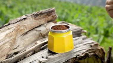 Kadın turist, çay kaşığıyla öğütülmüş kahveyi sarı moka demliğine koyup yaz kampında yeşil dağ kahvesi yapıyor. Sabah pikniği, doğada kahvaltıda sıcak içecek pişiren kişi..