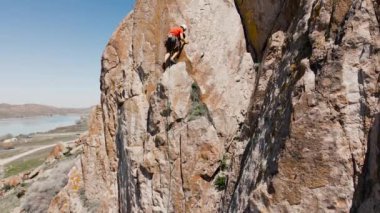 Orta Asya, Kazakistan 'daki Ili nehrindeki yüksek kayalıklara tırmanan turuncu tişörtlü bir adamın insansız hava aracı görüntüsü.