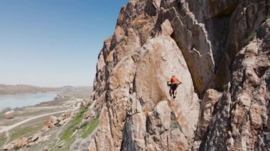 Orta Asya, Kazakistan 'daki Ili nehrindeki yüksek kayalıklara tırmanan turuncu tişörtlü bir adamın insansız hava aracı görüntüsü.