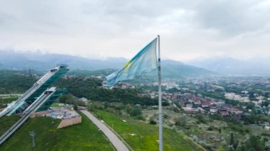Kazakistan 'ın başkenti Almaty' de kar dağlarına karşı Ulusal Kazakistan bayrağı ve trambolin atlama kompleksinin hava aracıyla yörünge görüntüsü.