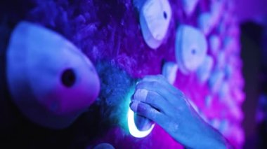 Spor salonundaki kayaya tırmanan adam, parlak mavi ve pembe ışıkla duvara tırmanıyor. Tutuşa yakın çekim yap.