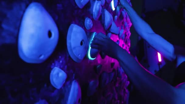 男子马拉松攀岩者室内攀岩墙 霓虹灯发出蓝光和粉色光 — 图库视频影像