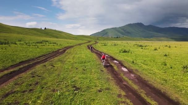 カザフスタンの美しい山の谷にある緑の丘の森の道でカップルライドマウンテンバイクの空中ドローンショット エクストリームスポーツ旅行バイクパックとアウトドアレクリエーション — ストック動画
