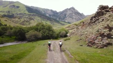 Kazakistan 'daki güzel kayalık dağ vadisinde yeşil tepe orman yolunda iki adamın hava aracı görüntüleri. Extreme Sport bisiklet paketleme ve açık hava eğlencesi.