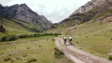 Kazakistan 'daki güzel kayalık dağ vadisinde yeşil tepe orman yolunda iki adamın hava aracı görüntüleri. Extreme Sport bisiklet paketleme ve açık hava eğlencesi.