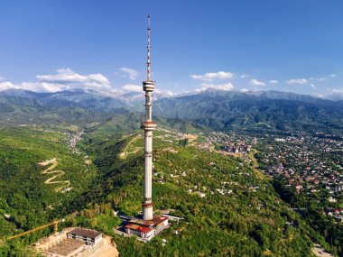 Sembol Almaty şehrinin yüksek televizyon kulesinin hava aracı görüntüsü ve Kazakistan 'daki kar dağlarına karşı Koktobe tepesine park