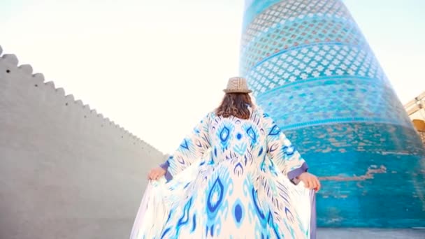 乌兹别克斯坦伊昌卡拉古镇Khiva市Minaret Kalta小东方建筑附近 身着蓝色图案民族服装的少女慢行 — 图库视频影像
