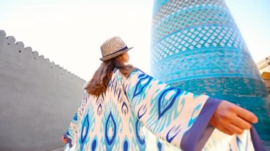 Özbekistan, Itchan Kala antik kenti Khiva 'da, Minaret kalta yakınlarında mavi desenli yavaş hareket eden genç bayan dans ediyor..