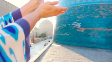 Özbekistan 'ın Itchan Kala antik kenti Khiva' daki küçük doğu binaları yakınlarında mavi desenli doğu danslı kadın yavaş çekim dansçısının ellerini kapatın..