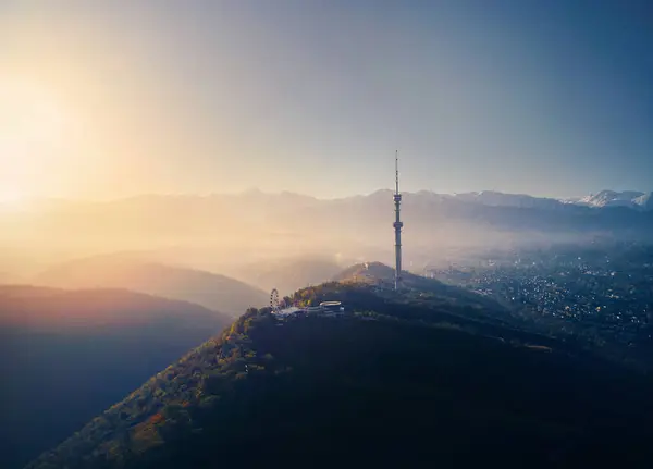 stock image Aerial drone shot of symbol Almaty city high TV tower and park at Koktobe hill against snow mountains at sunrise in Kazakhstan