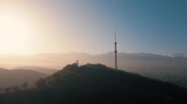 Sembol Almaty şehrinin yüksek televizyon kulesinin hava aracı görüntüsü ve Kazakistan 'da güneş doğarken Koktobe tepesine park etmek.