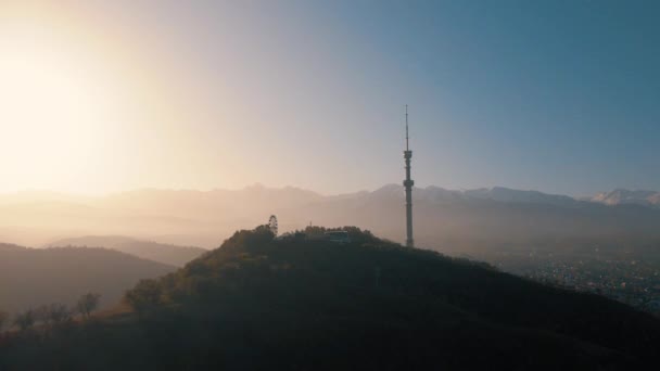 カザフスタンの日の出に雪山に対してコクトーベ丘のシンボル高いテレビ塔と公園の空中ドローンショット — ストック動画