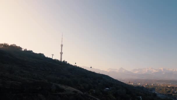 カザフスタンの日の出に雪山に対してコクトーベ丘のシンボル高いテレビ塔と公園の空中ドローンショット — ストック動画