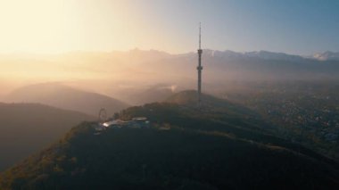 Sembol Almaty şehrinin yüksek televizyon kulesinin hava aracı görüntüsü ve Kazakistan 'da güneş doğarken Koktobe tepesine park etmek.