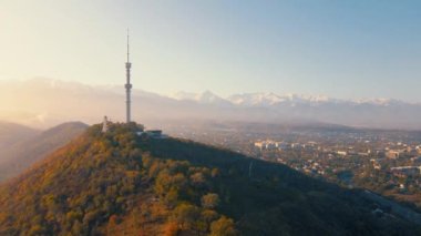Sembol Almaty şehrinin yüksek televizyon kulesinin hava aracı görüntüsü ve Kazakistan 'da güneş doğarken Koktobe tepesine park etmek.
