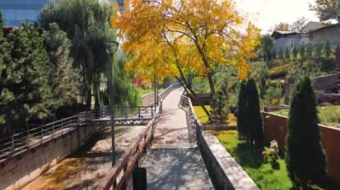 İnsansız hava aracı Almaty şehrinde sonbahar zamanı ağaçların yanındaki köprüden geçerken çekilen görüntüyü takip ediyor.