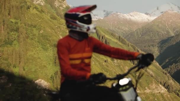 スノーマウンテンバックグラウンドで明るい光で電動バイクのフルフェイスヘルメットのフォーカスシルエットからマウンテンバイカーの肖像画 — ストック動画