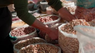 İnsan, Özbekistan 'ın Buhara kentindeki yerel gıda pazarında taze badem hasadı ve kurutulmuş meyveleri poşetlerde satıyor.
