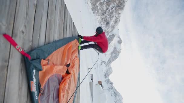 大胡子男子在冬季山区自然条件下搭建橙色帐篷作为户外度假避风港的垂直录像 度假和探险旅行概念 — 图库视频影像