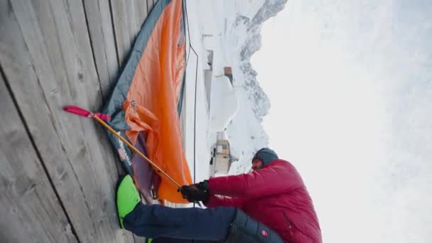大胡子男子在冬季山区自然条件下搭建橙色帐篷作为户外度假避风港的垂直录像 度假和探险旅行概念 — 图库视频影像