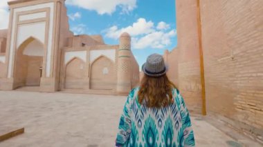 Madrassah meydanında yürüyen mavi süslemeli ve şapkalı genç kadın portresi. Özbekistan 'ın antik Khiva kenti Itchan Kala.