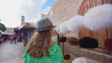 Yeşil elbiseli ve şapkalı genç bir kadın pazar ve minare meydanında yürüyor. Özbekistan 'ın antik Khiva kenti Itchan Kala.