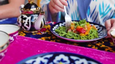Shivit osh Khorezm lagman yeşil erişte yiyen kadın Özbek mutfağının ulusal yemeklerinden et ve sebzeli. Özbekistan 'ın Khiva kentindeki restoranda geleneksel süs tabakları ve tabaklar