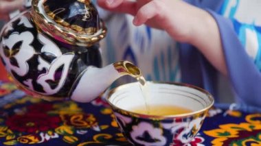 Özbekistan 'ın Khiva kentindeki restoranda fincana mavi doğulu geleneksel süs eşyasıyla çayını dolduran kadın.
