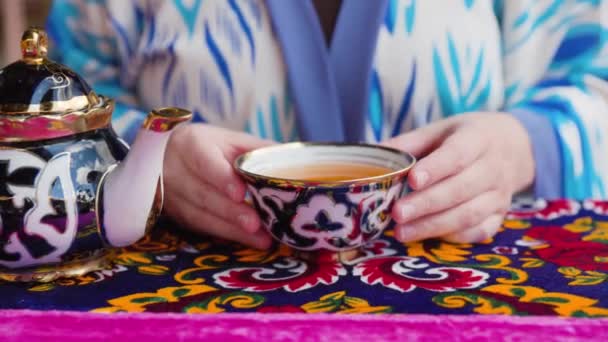 ウズベキスタンのキバのレストランでカップで青い東洋の伝統的な装飾と鍋から紅茶を飲む女性 — ストック動画