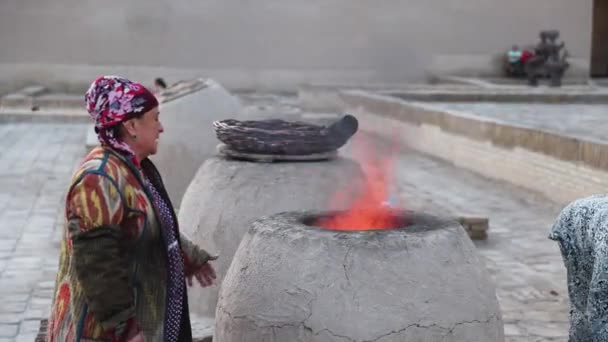 キヴァ オスベキスタン 伝統的なドレスの女性はタンドールオーブンで火とパンを作ります — ストック動画