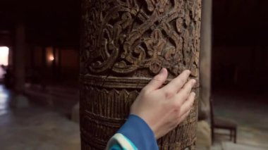 Etnik elbiseli turist kadın Juma Camii, Khiva, Özbekistan 'daki tahta oyma sütunlara dokundu.