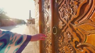 Mavi süslemeli etnik giysili genç bir kadın eski ahşap kapıyı açmaya çalışıyor. Özbekistan 'daki Itchan Kala antik şehir Khiva' nın sokak pazarı.