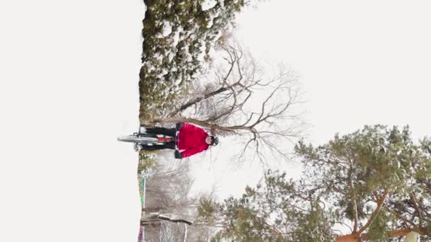Függőleges Videó Egy Piros Kabátos Férfiról Aki Havas Parkban Biciklizik Stock Videó