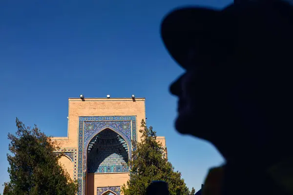ウズベキスタンのサマルカンドの青空に対してタマレーン アミールの古い建物Gur Emir Mausoleumの側面のプロフィールのシルエットそして外観に直面する女性 ロイヤリティフリーのストック画像