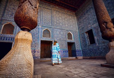 Tash Hauli 'deki mavi mozaik saray binasının iç avlusunda etnik giyinmiş kadın turist Özbekistan' ın Khiva kentindeki ahşap kolona sahip..