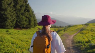 Sırt çantalı ve şapkalı bir kadın gezgin dağlarda ve ormanda yürüyor. Yolculuk konsepti atmosferik destansı an.