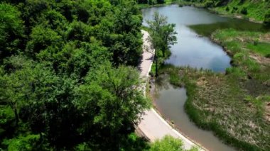Sarı ceketli bisikletçi güneşli bir günde küçük göl kenarında kırsal yolda at sürüyor. Bisiklet turizmi kavramı.