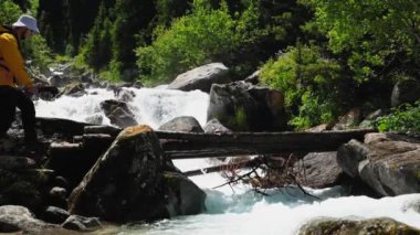 Sarı ceketli Yürüyüşçü, Orta Asya, Kazakistan 'da, beyaz su dağı nehrine karşı köprüyü yavaş çekimde geçiyor.